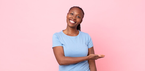 afro black adult woman smiling cheerfully, feeling happy and showing a concept in copy space with palm of hand