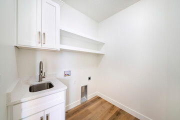 Empty white laundry room with top storage, laundry connections and dryer vent on the wall
