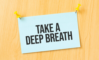 Take a deep breath sign written on sticky note pinned on wooden wall