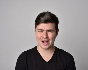 Fototapeta premium Close up head and shoulders portrait of a brunette. young man with a variety of expressive facial expressions. Isolated on a light grey studio background.