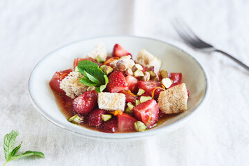 Delicious summer salad. Salad bowl with strawberries, tomatoes, pistachios and croutons in honey orange oil sauce on beige linen tablecloth