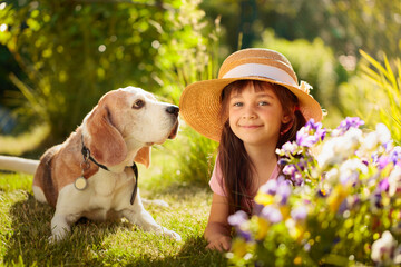 Happy little girl in a straw hat playing with his pet on the grass in the garden.