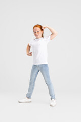 Beautiful cute little red-headed girl in casual outfit having fun isolated on white studio background. Happy childhood concept. Sunny child