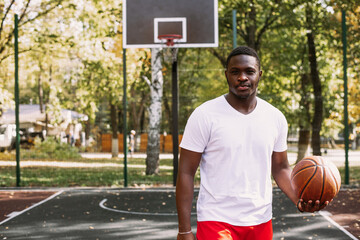 Portrait of a handsome black young man holding a basketball on a basketball court. Take a break during your workout. Fashionable sports portrait