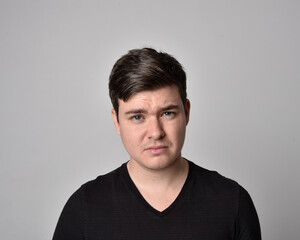 Fototapeta premium Close up head and shoulders portrait of a brunette. young man with a variety of expressive facial expressions. Isolated on a light grey studio background.