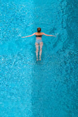 A beautiful girl is swimming in the clear water of the pool. Rest at the hotel. Summer holidays. 