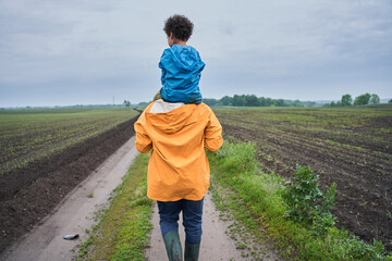 Boy is sitting at the shoulders of his father and embracing his parent