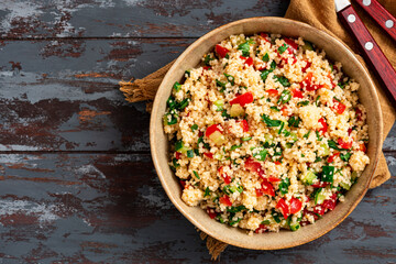 Vegan salad made of couscous, tomatoes, cucumbers, parsley and lemon juice. Couscous with vegetables in a bowl on a dark wooden background. Tabbouleh salad.