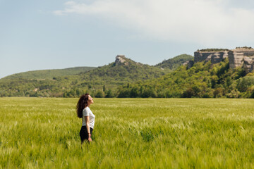 Fototapeta na wymiar beautiful brunette woman walking through a field of wheat looks at the nature