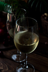White wine is poured into glasses. There are fruits nearby