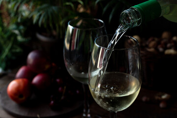 White wine is poured into glasses. There are fruits nearby
