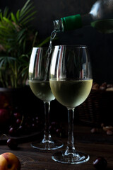 White wine is poured into glasses. There are fruits nearby