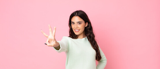 young pretty woman smiling and looking friendly, showing number three or third with hand forward,...