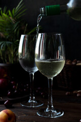 White wine is poured into glasses. There are fruits nearby