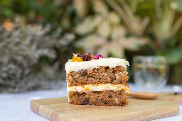 Carrot cake with walnuts, prunes and dried apricots on a wooden tray in warm sunlight at garden tree on background.