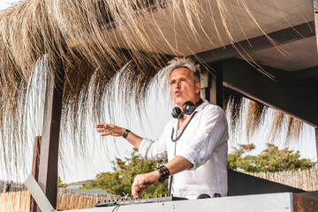 Disc jockey playing music for tourist people at club party outdoors on the beach - Dj wearing...