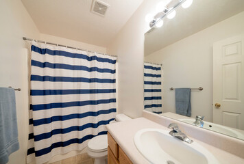 Interior of a bathroom with vanity sink and closed blue and white striped shower curtain