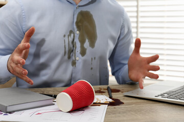 Man with spilled coffee over his workplace and shirt, closeup