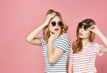 two girlfriends stand side by side in striped t-shirts glasses fashion summer pink background