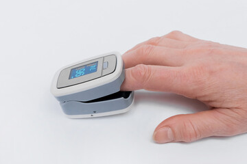 An elderly woman's arm is close-up measuring blood oxygen levels with her finger in a pulse oximeter on a white background