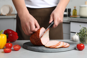 Man cutting delicious ham at grey table indoors, closeup
