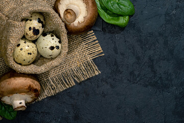 Quail Eggs Placed  Into The Coarse Cloth Pouch. Royal Mushrooms And Leaves Of Spinach Are Near Them.  Slate Black Uneven Stone Background. Close Up. Top View. Free Space For Text Or Menu. Eco Concept.