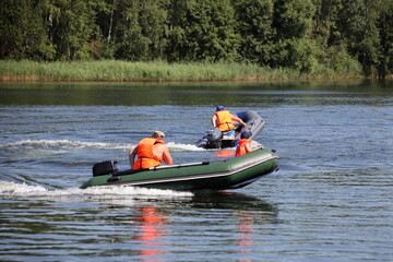 Two inflatable motor boats with outboard motors and  people in orange lifejackets fast floating on...