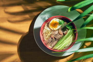 Spicy Asian Sichuan soup with noodles, beef, egg and cucumber in a bowl.