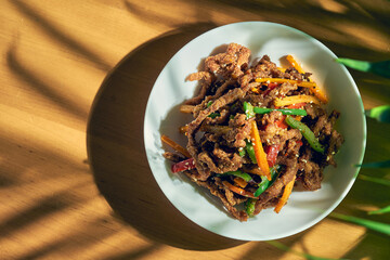 Spicy dry Sichuan wok beef with pepper, sesame seeds, carrots and green tomato in a white bowl. Chinese cuisine