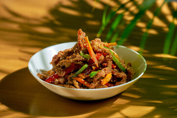 Spicy dry Sichuan wok beef with pepper, sesame seeds, carrots and green tomato in a white bowl. Chinese cuisine