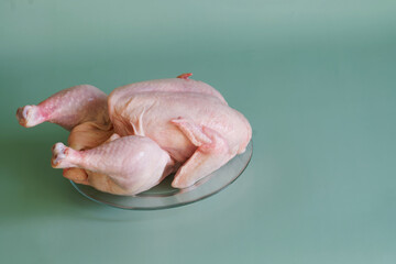Raw chilled gutted chicken in a transparent plate on a green background