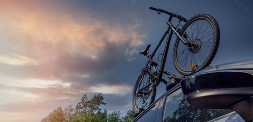 bicycle on the car roof rack against sunset sky. copy space