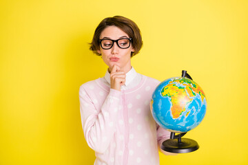 Photo portrait female student in spectacles thoughtful looking at globe isolated vibrant yellow color background