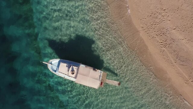 Aerial view of the white yacht in the clear turquoise water on sandy beach.