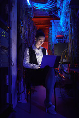 Vertical portrait of young female technician setting up internet network in server room