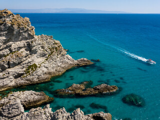 Aerial view of moored boats floating on a transparent sea. Scuba diving and summer holidays. Capo Vaticano, Calabria, Italy. Promontory.
