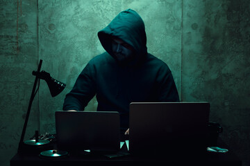 Anonymous hacker wearing face mask working on computer in dark room