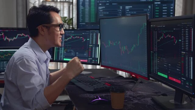 Asian Male Stock Market Broker Happy With Analyzing Graphs On Multiple Computer Screens 
