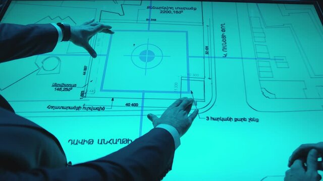 Two men in black suits meeting at dark office room and using a modern, futuristic big touch screen tablet. Businessmen looking at map illuminated on digital table, discussing and talking . Slow Motion