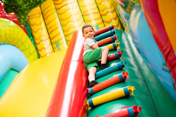 Little boy child climbs the stairs of a multi-colored slide in the park. - obrazy, fototapety, plakaty