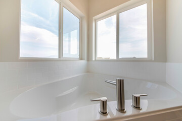 Corner bathtub in a bathroom with widespread faucet against the windows
