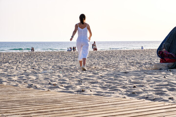 Chica joven vestida de blanco caminando sola por la orilla de playa al atardecer