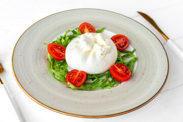 Salad with burrata cheese and cherry tomatoes on white wooden background