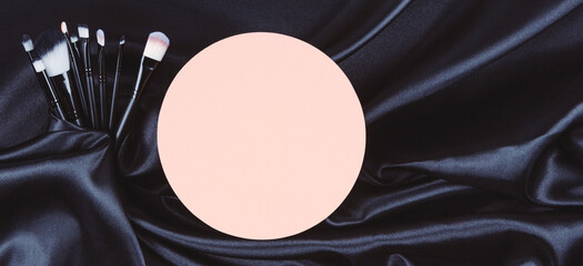 Make-up cosmetic brushes and pastel round blank podium platform on black wavy silk background. Beauty, skin care and fashion concept. Top view