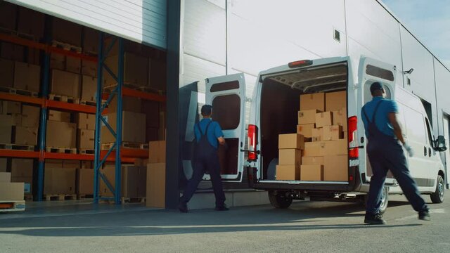 Outside of Logistics Distributions Warehouse: Two Workers Load Delivery Truck with Cardboard Boxes, Drive Off to Deliver Online Orders, Purchases, E-Commerce Goods. Wide Shot