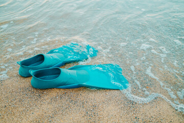 Pair of teal flippers on sandy sea or ocean beach, side view. Swimming equipment - fins on shore....