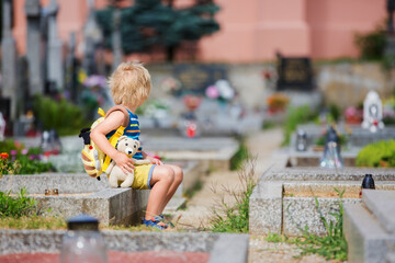 Little toddlet boy, sitting on a cemetery, feeling sad
