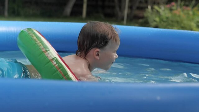 Funny baby boy floating in safety buoy watermelon surrounded by water splashing side view