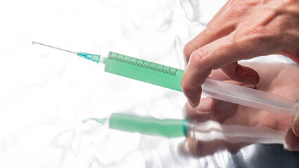
hand with syringe and needle, with green injection on mirror background