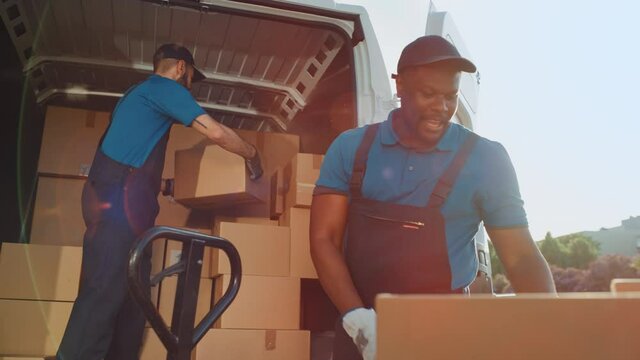 Logistics Warehouse Two Happy Workers Talk, Joke use Hand Pallet Truck Start Loading Delivery Truck with Cardboard Boxes, Online Orders, Purchases, E-Commerce Goods. Slow Motion Low Angle